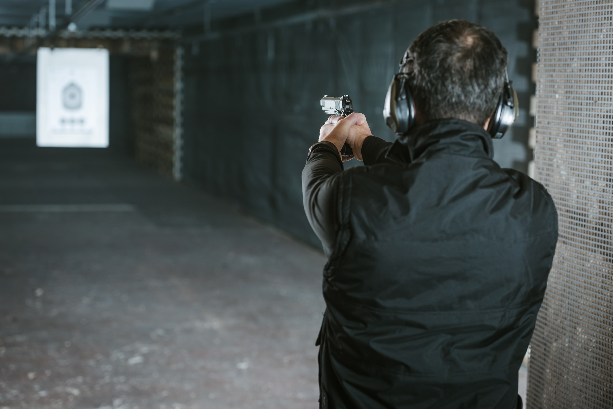 rear-view-of-man-aiming-gun-at-target-in-shooting-range.jpg
